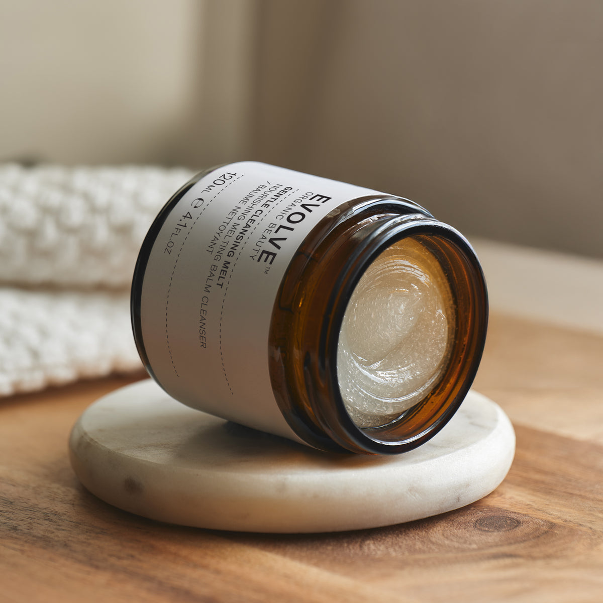Open jar of Evolve Gentle Cleansing Melt 120ml, displaying the smooth texture of the cleansing balm. The jar is lying down on its side on a marble coaster with a neutral background