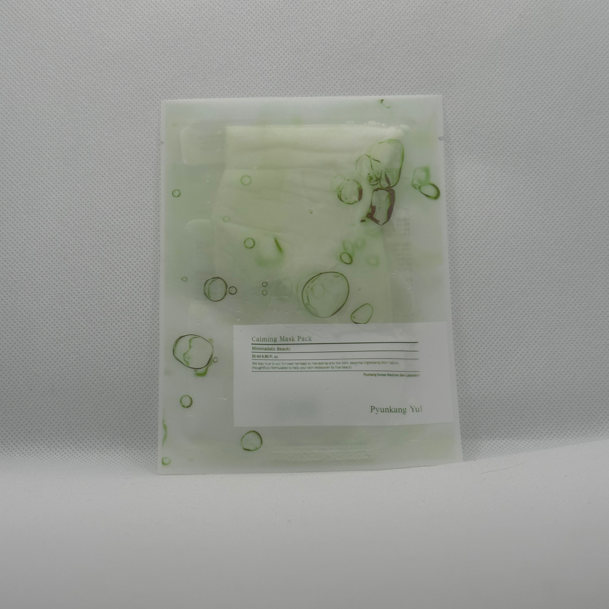 Pyunkang Yul Calming Mask 25ml. A translucent white sheet mask pouch with green circular patterns and a white label, photographed on a light gray textured background.