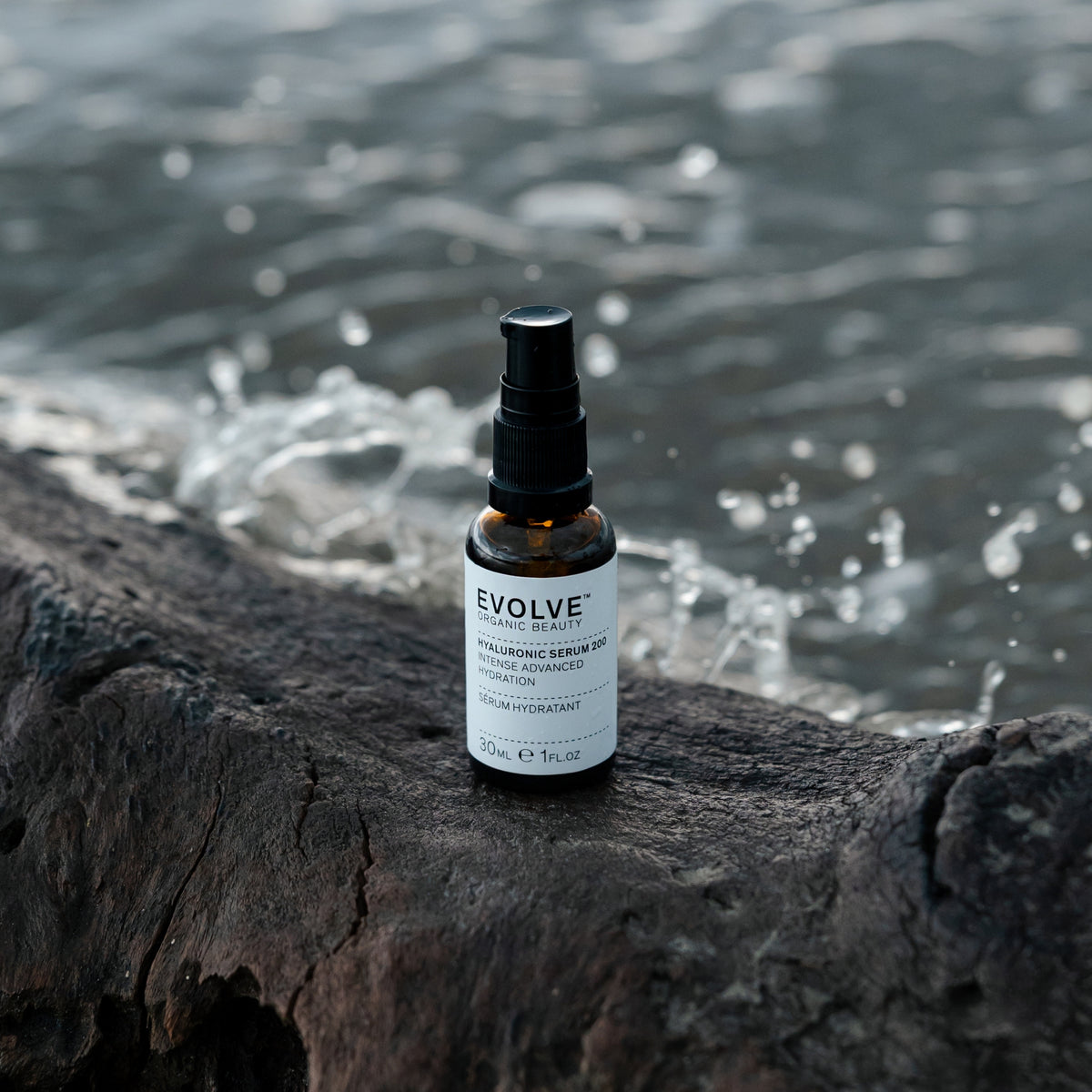Evolve Hyaluronic Serum 200 30ml bottle on a dark wood with water splashing in the background.